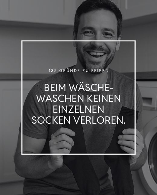Mann hält zwei Socken und kniet vor der Waschmaschine