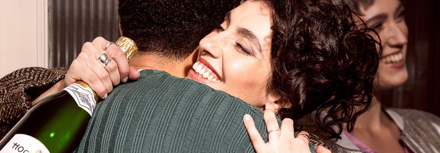 Eine Dame umarmt einen Mann und hält eine Hochriegl Flasche in der Hand