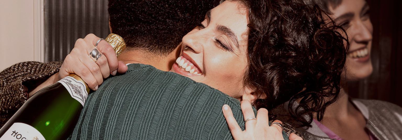 Eine Frau umarmt einen Mann und hat dabei eine Flasche Hochriegl in der Hand