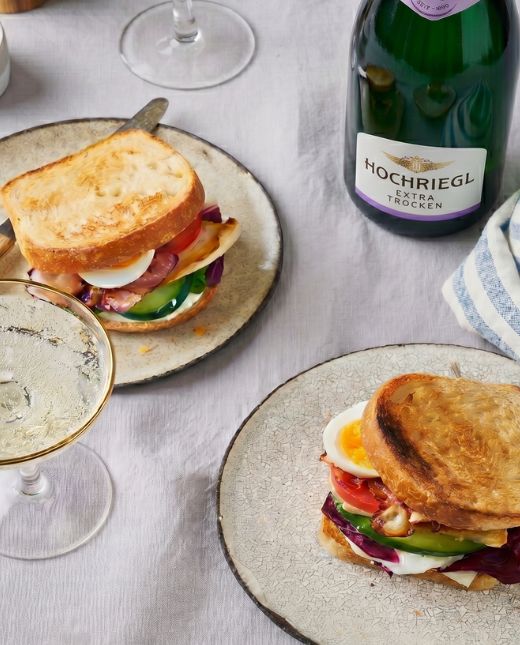 Eine Flasche Extra Trocken Hochriegl, Sektschalen und zwei Sandwiches auf einem Tisch