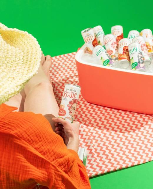 Dame mit Strohhut sitz auf Picknickdecke und hält eine Dose Rosie Spritz in der Hand