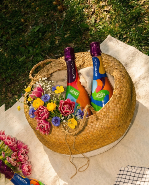 Zwei Flaschen Love Edition liegen mit Blumen in einem Picknickkorb