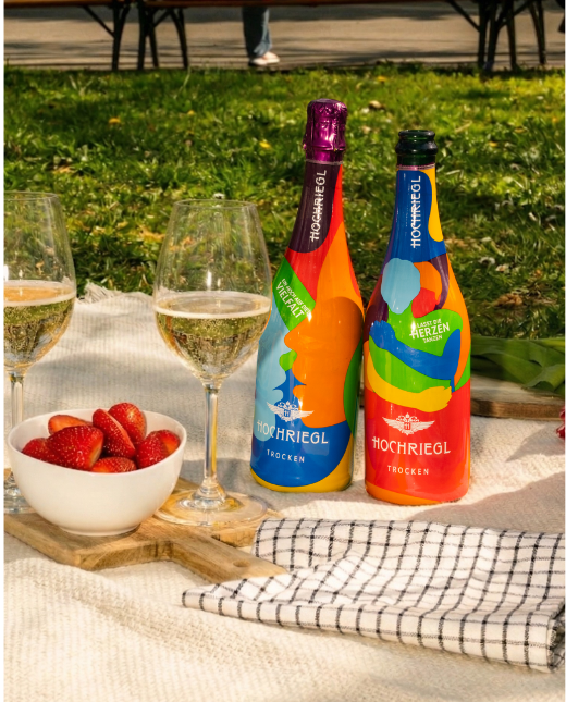 Zwei Flaschen Hochriegl Love Editions und zwei gefüllte Gläser stehen auf einer Picknickdecke mit Erdbeeren