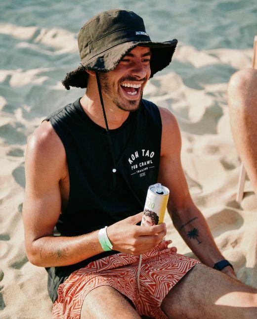 Mann sitzt im Sand und trink eine Hochriegl Spritz Lorenzo